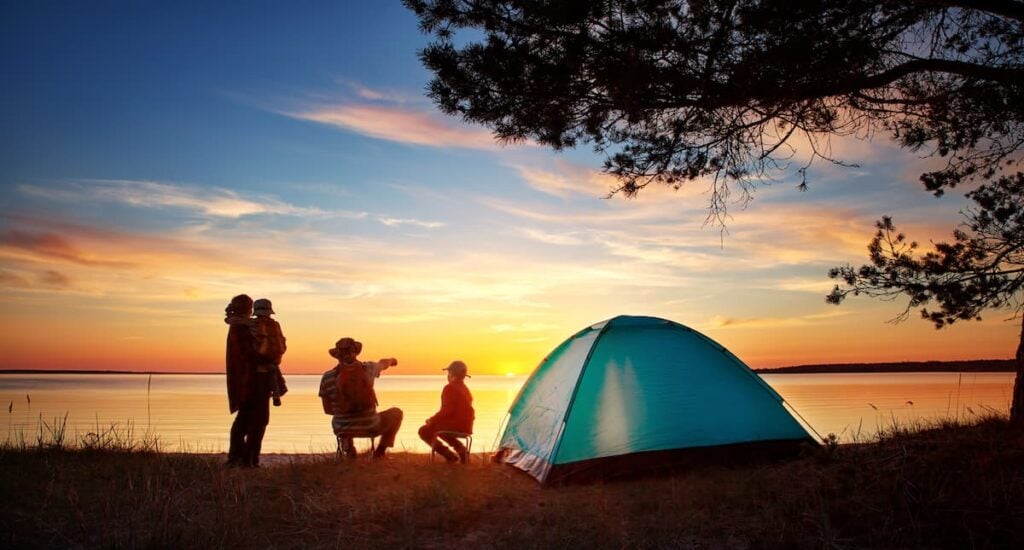 A family of four fishing by a pitched tent at sunset