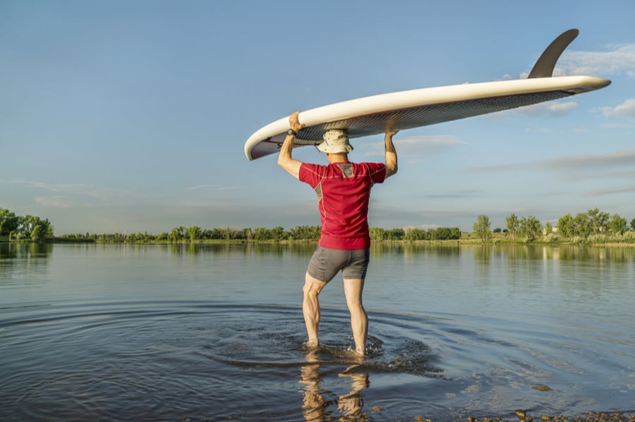 Ultimate Beginner’s Guide to Stand Up Paddleboarding (SUP) 6 Man Hauling Stand Up Paddleboard Into Water