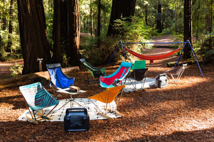 Campsite setup with chairs, hammock, and tent heater in forest.