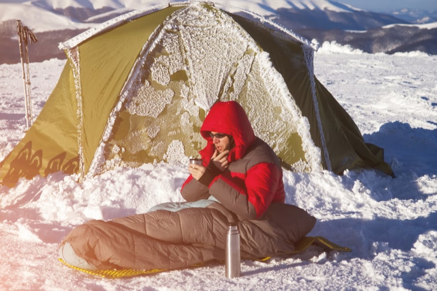 Man in Sleeping Bag Outside in Snow in Front of Tent