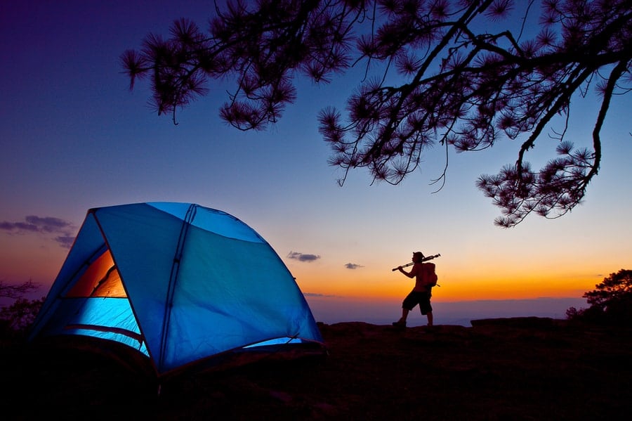 Man standing near camping tent at sunset.