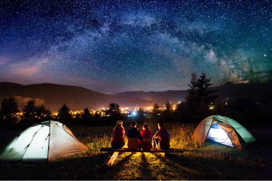 Group of campers near camping tents looking at Milky Way at night.