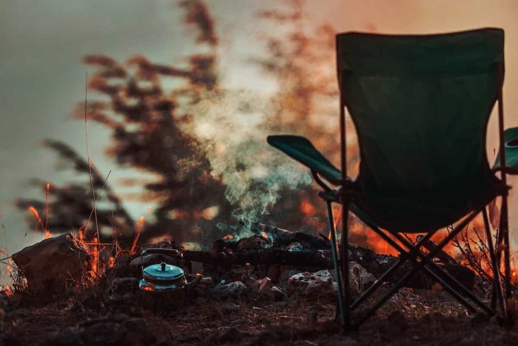 A camping chair set up near a campfire at sunset.