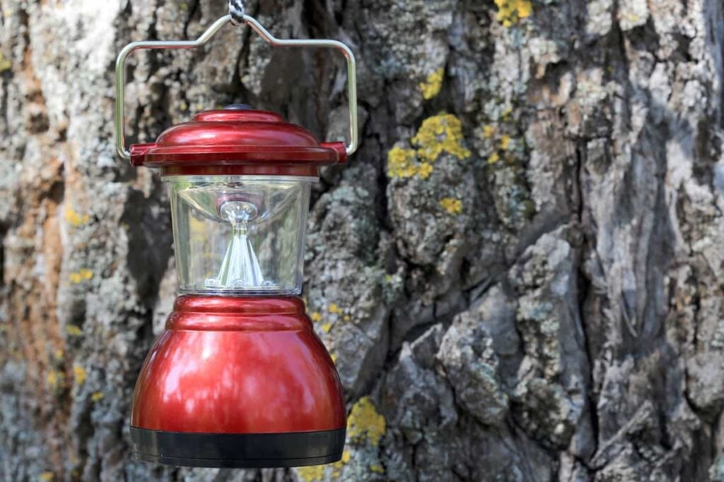 A camping lantern hanging near a tree.