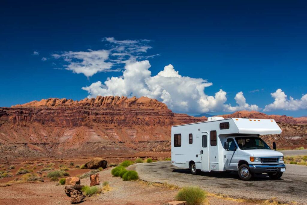 An RV in a desert setting with red rock mountains in the background.