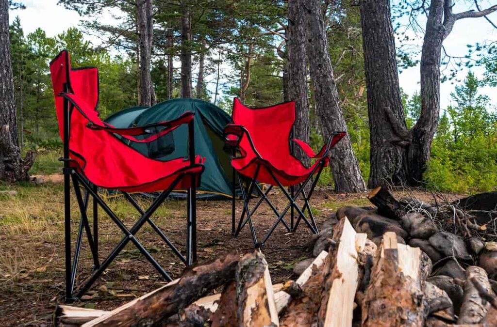 A tent campsite with red camping chairs set up near a campfire.