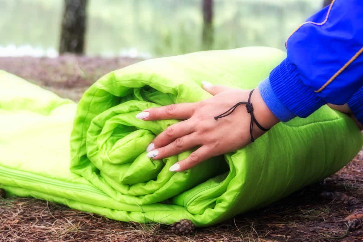 How to Choose the Right Camping Bed: A Comprehensive Guide 6 A woman rolling up a green sleeping bag.