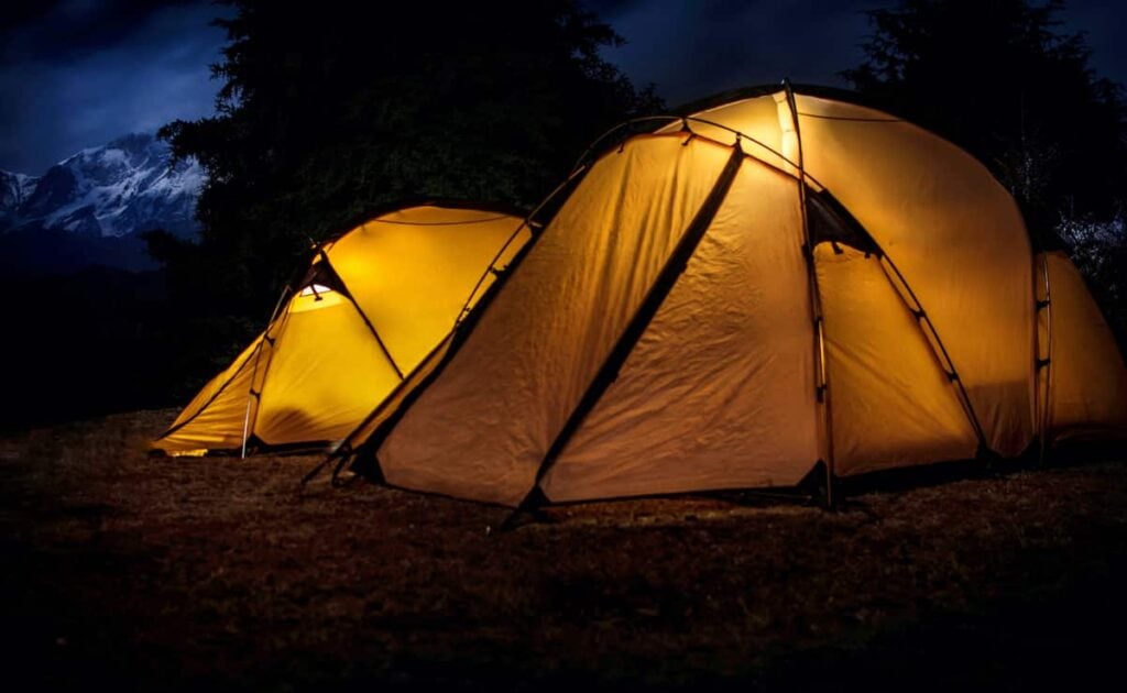 Two yellow tents lit from within by lanterns at night. The best solar lights for camping make nighttime hours more enjoyable.