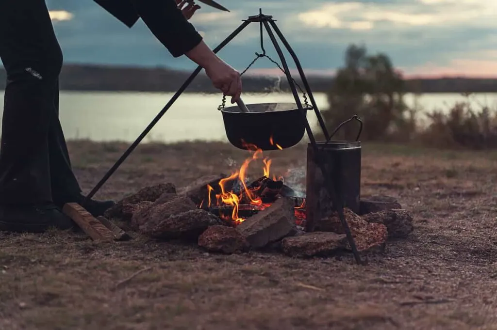 Camping for Beginners: How to Set Up a Tent and Stay Comfortable 5 Person cooking in a Dutch oven hanging over a campfire.
