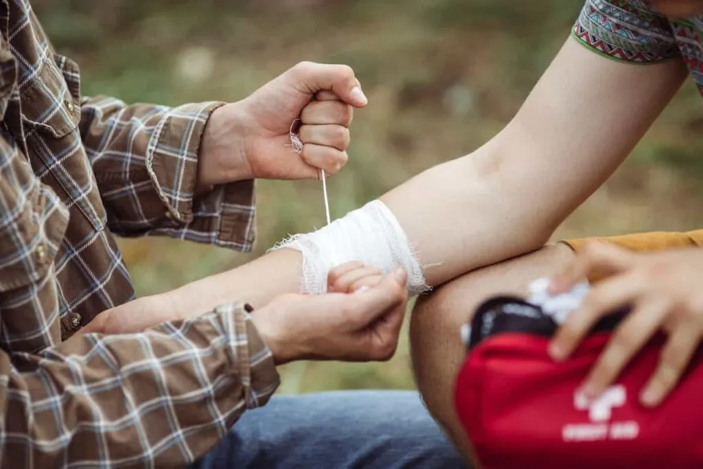 Camping for Beginners: How to Set Up a Tent and Stay Comfortable 6 Person bandaging another person's arm. Camping first aid concept.