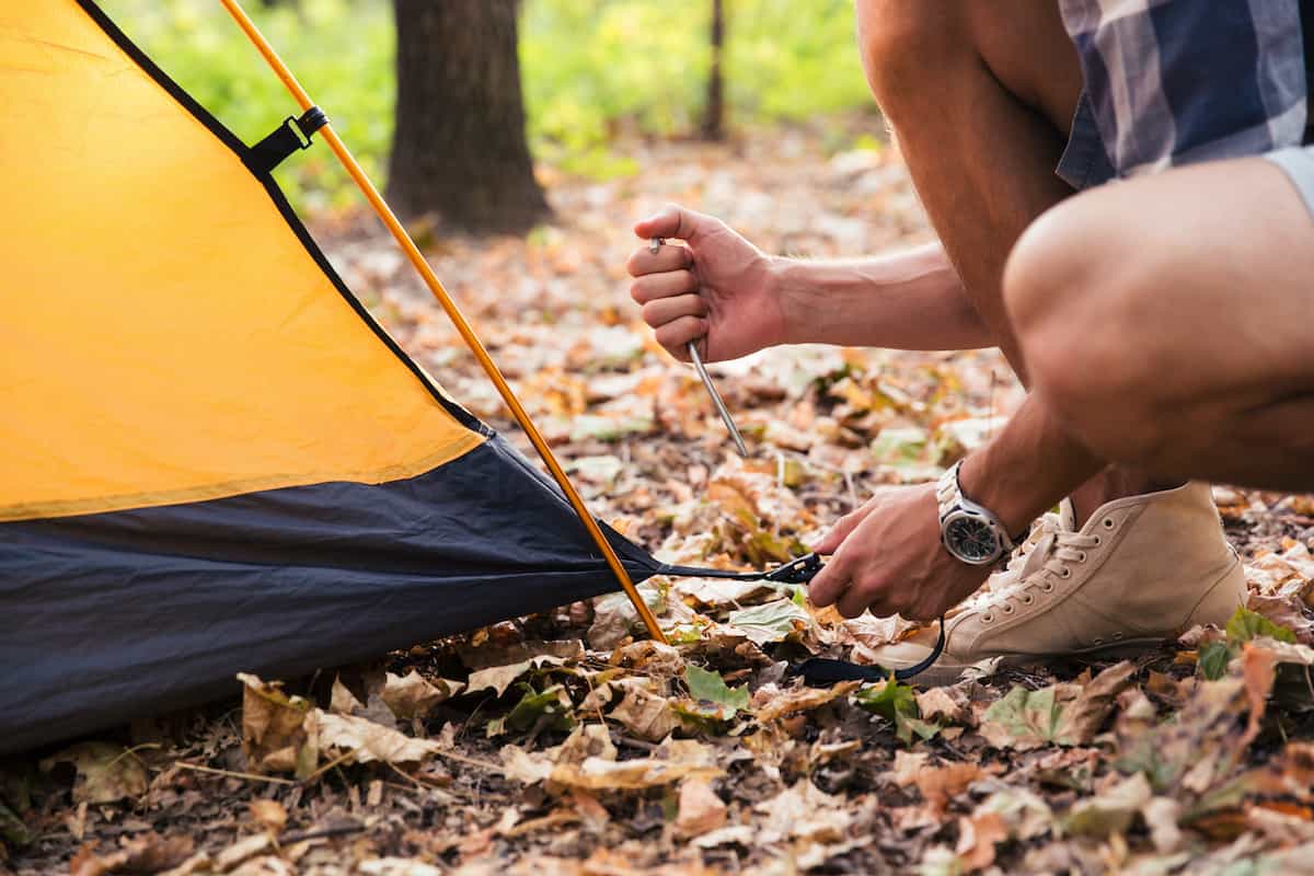 What is a Tent Footprint and Why You Need One 5 Person securing corner of tent with tent stakes.