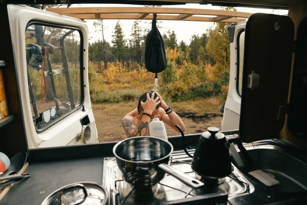 Going Green: The Best Solar Camping Gear for Sustainable Adventures 11 A man using a hanging camp shower, another solar camping gear item.