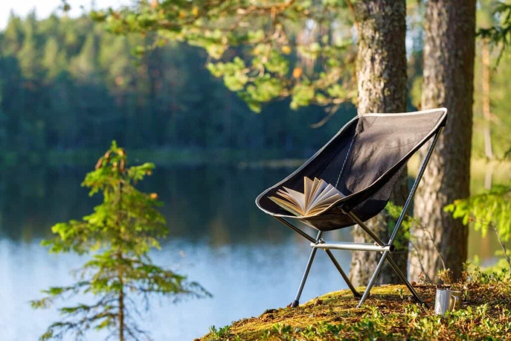 A backpacking chair by a lake with a book lying on the seat.