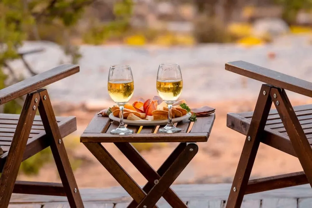 The 12 Best Spots for Glamping in the Grand Canyon 5 Outdoor chairs and a small table set with wine glasses and a charcuterie plate.
