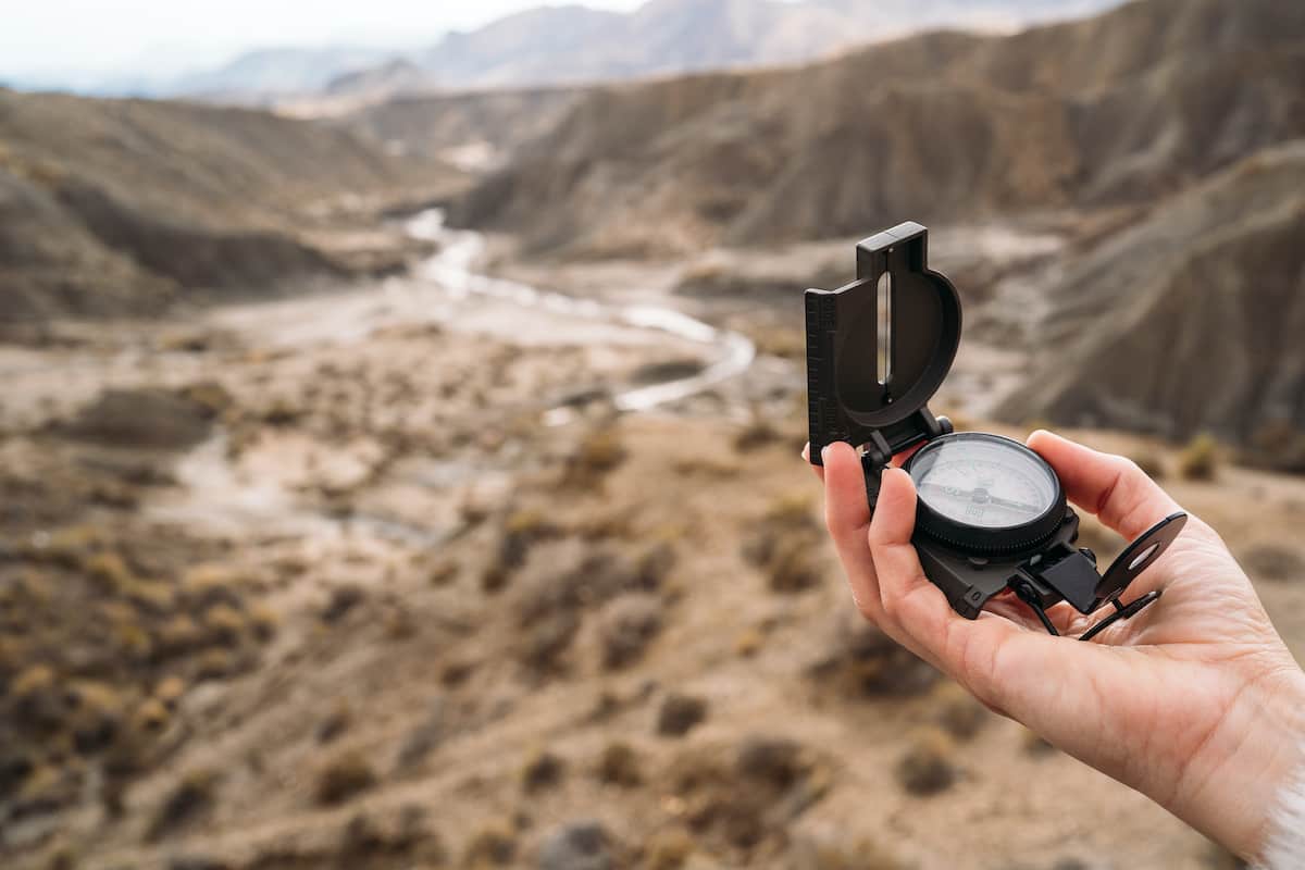 10 Dicas para Acampar no Deserto 4 Pessoa segurando uma bússola com cenário de deserto ao fundo.
