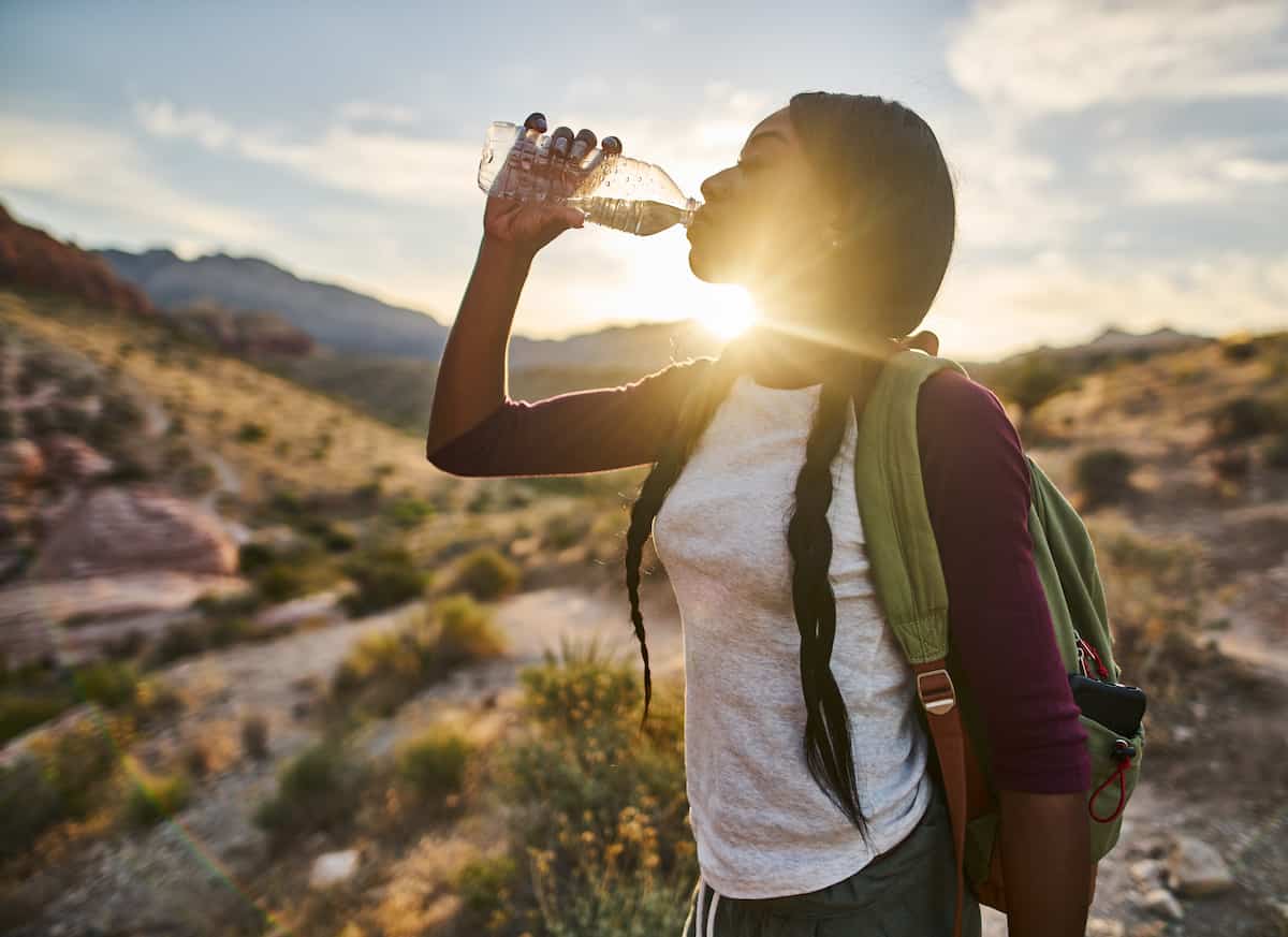 10 dicas para acampar no deserto 2 Mulher em uma paisagem desértica bebendo água enquanto caminhava.