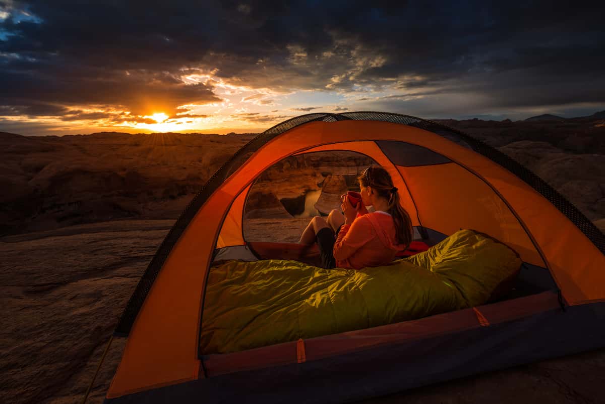 10 Dicas para Acampar no Deserto 12 Uma mulher desfrutando de um café e observando o nascer do sol no deserto em sua barraca.