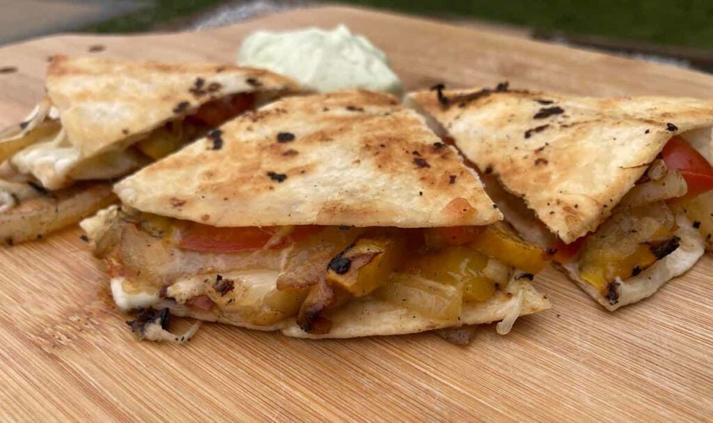 Closeup of finished vegetable quesadilla cut into wedges with dipping sauce in background.