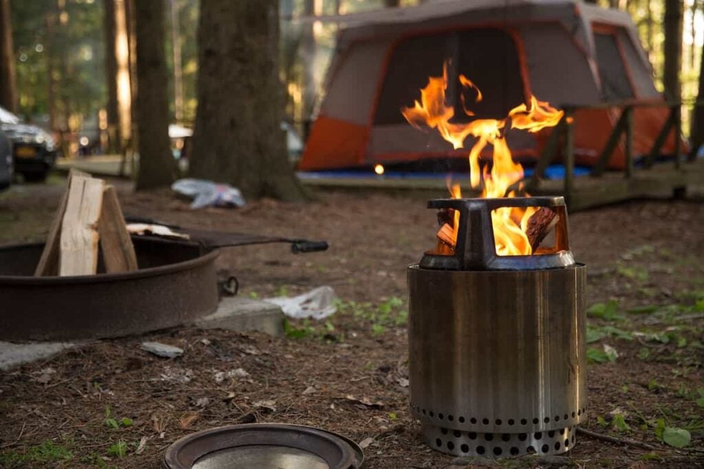 A tent campsite with a portable wood stove fire.