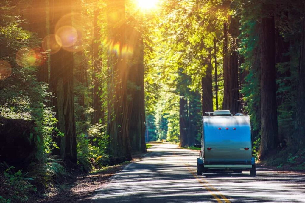 A small trailer camper being pulled along a wooded highway.