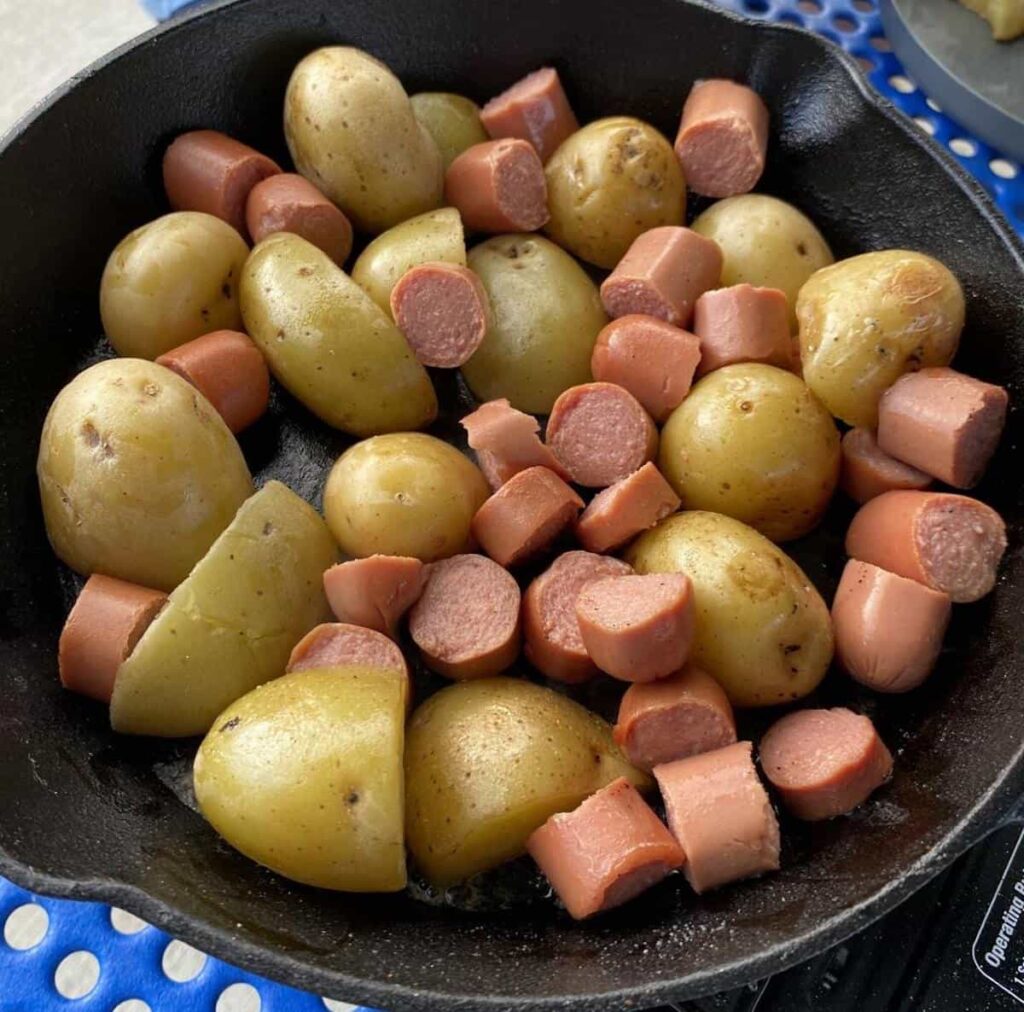 How to Make Campfire Potatoes 3 Potatoes and sliced hotdogs in a cast iron skillet.