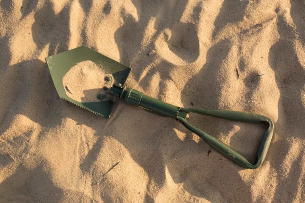The Best Camping Shovel: Our Top 5 Picks 10 A green camping shovel lying on sand.