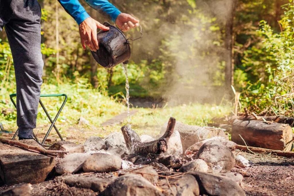 8 Tips for Finding the Perfect Campsite 6 Person pouring water on a campfire.