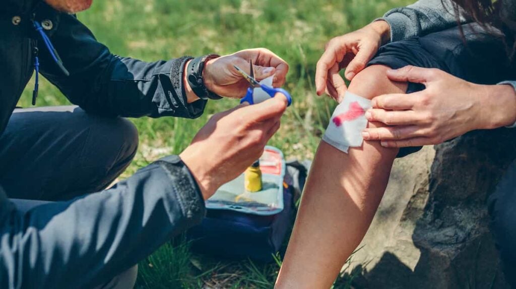 如何制作背包急救箱 4 正在对膝盖受伤流血的徒步旅行者进行急救的人员。