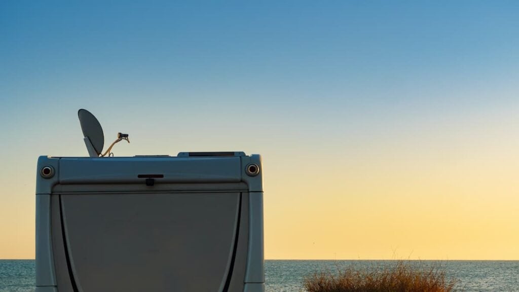 Stay Connected: Reviewing the Best RV Satellite Internet Options 4 An RV with a satellite dish on the roof parked by the ocean.