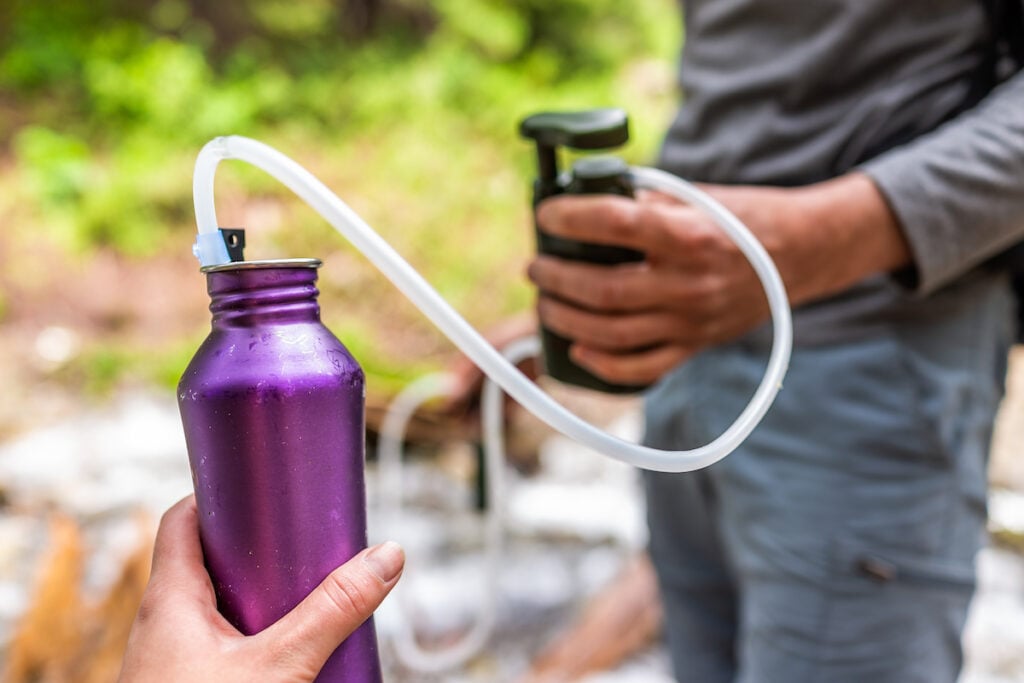 Man and woman couple using water filter on hiking trail river in Colorado to purify drinking water into bottle